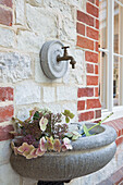 Victorian tap and basin with cut flowers on exterior of renovated schoolhouse West Sussex England UK