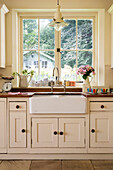 Cream cupboards and butler sink at uncurtained kitchen window in renovated Victorian schoolhouse West Sussex England UK