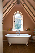 Freestanding bath below arched window in attic conversion of Victorian schoolhouse West Sussex England UK