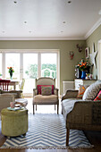 Sofa und Sessel mit geknöpftem Fußhocker und gemustertem Teppich im Wohnzimmer eines Hauses in Großbritannien