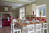White barstools at wooden kitchen worktop in brightly tiled kitchen of UK home