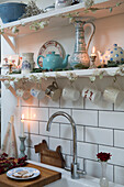 Cups hanging on shelf hooks with crockery in London kitchen England UK