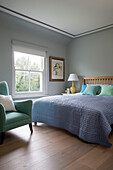 Lilac quilt with light green armchair at bedroom window in modernised Victorian cottage Sussex England UK