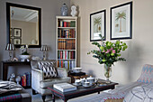 Grey armchair and bookcase with framed prints and cut flowers in London townhouse apartment UK