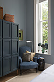 Blue armchair and teal wardrobe at window in bedroom of London townhouse UK