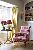 Pink upholstered armchair and pedestal base side table in bay window of Sussex home England UK