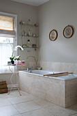 Orchid at side of bath with vintage wall mounted shelf in Sussex bathroom England UK