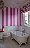 Freistehende Badewanne unter dem Fenster mit rosa gestreifter Tapete in einem Badezimmer in Südlondon, England UK