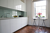 Pink Peonies (Paeonia) and bar stools in white fitted kitchen with parquet flooring in London townhouse England UK
