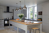 Brushed stainless steel pendant lights above long wooden table in Gloucestershire home England UK