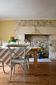 Painted chair and striped tablecloth with exposed stone fireplace in Gloucestershire farmhouse England UK