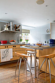 Wooden barstools at stainless steel breakfast bar in Gloucestershire farmhouse kitchen England UK