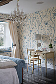 Light blue footboard with dressing table at window in papered bedroom of Gloucestershire farmhouse England UK