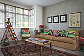 Step ladder at window in living room with vintage coffee table and bright scatter cushions in London home England UK