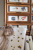 Fur throw on chair upholstered with bee with glass fronted draper's cabinet in Kelso home Scotland UK