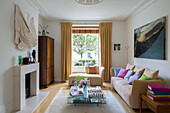 Kunstinstallation über dem Kamin mit niedrigem Glas-Couchtisch und beigen Sofas im Wohnzimmer eines Londoner Stadthauses England UK