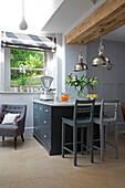 Bar stools at kitchen island with chrome pendant lights in Gloucestershire home England UK