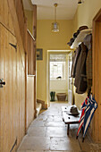 Coats hang in yellow hallway interior with flagstone flooring Gloucestershire England UK