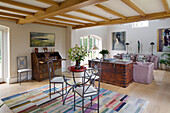 Glass topped table with metal chairs and patterned rug in open plan living room of Gloucestershire farmhouse England UK
