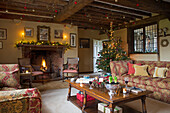 Entzündetes Feuer und Weihnachtsbaum mit Dekoration im Deckengebälk des Wohnzimmers in einem Bauernhaus in Hampshire England UK