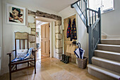 Antique chair with coats and boots in entrance hallway of Gloucestershire cottage UK