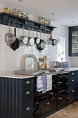 Storage jars on shelf with pans above black stove with dishcloths in Gloucestershire kitchen UK