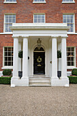 Black front door in portico entrance to brick country house Kent England UK