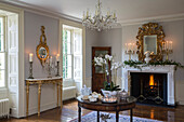 Orchid on polished antique table with gilt mirrors and lit fire in Kent country house England UK