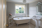 Freestanding claw-foot bath below window with pedestal basin in Kent country house England UK