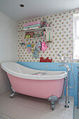 Retro- style pink freestanding bath below shelving in Victorian terraced cottage Kidderminster Worcestershire England UK