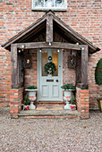 Light green front door with Christmas wreath in timber framed porch entrance of detached Cheshire home UK
