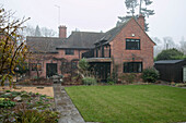 Wet footpath an lawn with brick exterior of detached Berkshire home in winter UK