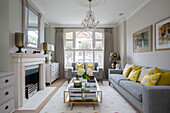 Gelbe Kissen auf grauen Sofas mit Vintage-Couchtisch im Wohnzimmer eines Londoner Stadthauses (UK)