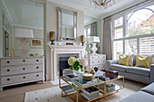 Pair of lamps in mirrored recess with chests of drawers and hydrangea on coffee table in London townhouse UK