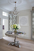 Chandelier above ceiling rose with books on table in hallway of London townhouse UK