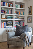Book storage with armchair and cushion in West Sussex home