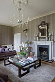 Glass topped coffee table on cream rug under chandelier in living room of Sussex country house UK