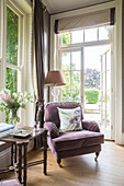 Floral cushion on armchair with lamp at open back door of detached Sussex country house UK