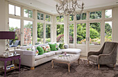 Armchair and white corner sofa with brown rug in conservatory windows of detached Sussex country house UK