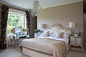 Cream double bed with mirrored dressing table at window in detached Sussex country house UK