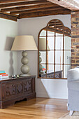 Large lamp on carved wooden trunk with salvaged mirror in Oast house conversion Kent UK