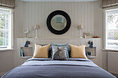 Black circular mirror on panelled wall above double bed in Oast house conversion Kent UK