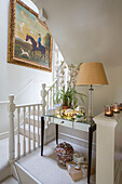 Gilt framed artwork with lamp on side table below stairs in London townhouse UK