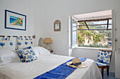 Sonnenhut auf dem Bett mit blauen Blumenkissen in einer italienischen Villa mit Blick durch das Fenster auf die Amalfiküste