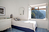 Sonnenbeschienenes Einzelbett mit Blick durch ein offenes Fenster in einer italienischen Villa an der Amalfiküste