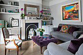 Ornaments on shelving with purple velvet cushions on grey sofas in London home UK