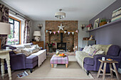 Purple sofas with exposed brick fireplace in living room of detached 1950s house Alford Surrey UK