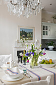 Cut flowers and fruit on dining table below glass chandelier in West Sussex townhouse UK