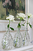 White single stem roses in glass vases on shelf with artwork in West Sussex townhouse UK