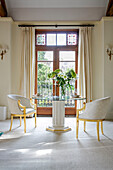 Pair of gilt chairs at glass topped table in double doorway of West Sussex townhouse UK